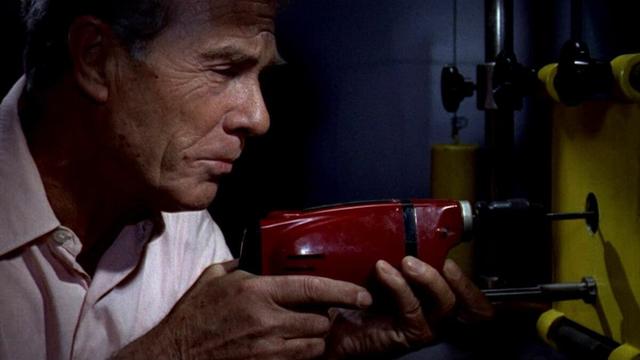 A man in a white shirt using a drill to crack a safe