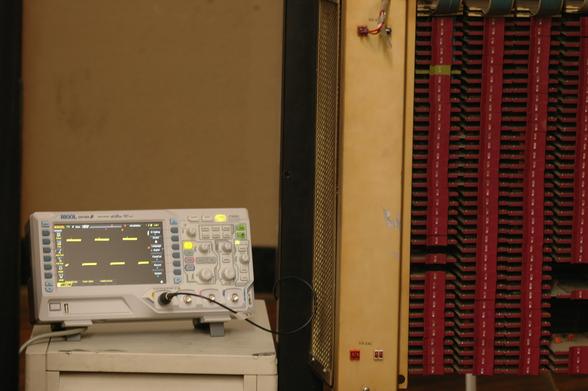 An oscilloscope displaying a simple waveform next to the insides of a late 60s computer.