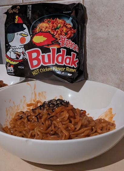 Cooked Buldak Korean noodles in a bowl with packet on display.