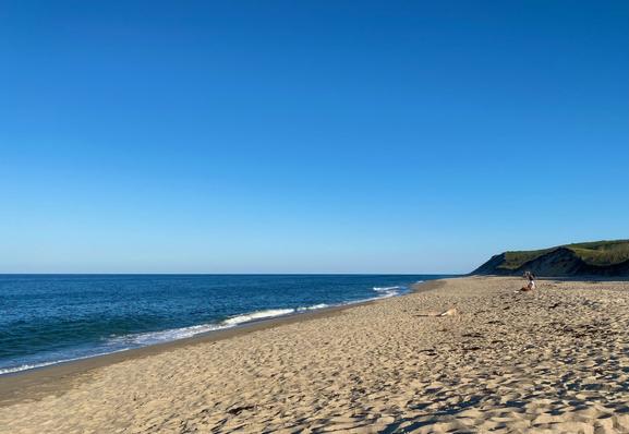 A white sandy beach recedes into the distance with deep blue ocean stretches to the left. Overhead, a crystal clear blue sky fades from light blue at the horizon where sand and sea meet, to deeper blue overhead.