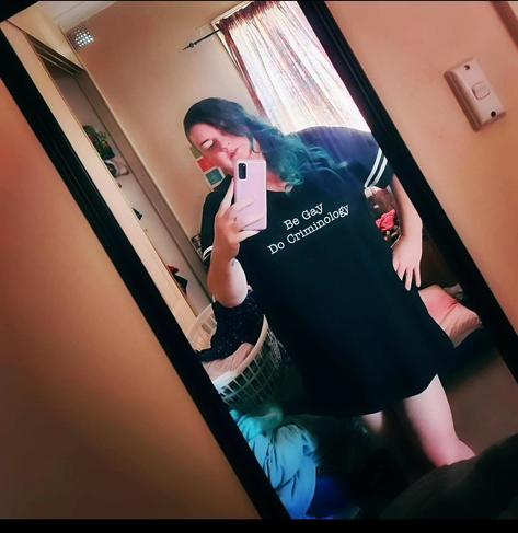 A selfie of me, wearing an oversized tshirt. It says "Be Gay. Do Criminology".