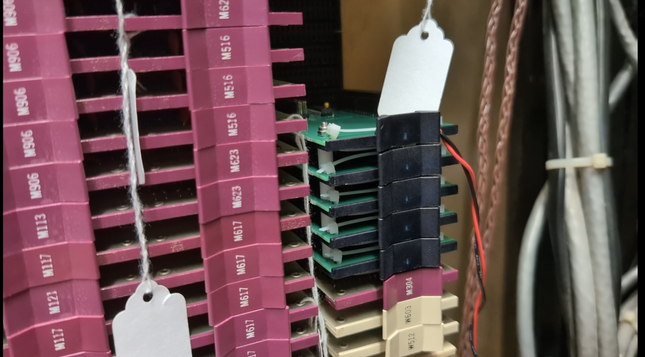 A five-card stack of printed circuit boards is visible plugged into the back plane of the PDP-12. A large number of other flip chip cards are visible plugged into the back plane. They have maroon handles with model numbers etched into them, while the five card stack has black 3D-printed handles.