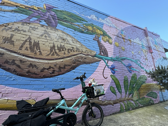 Two chihuahuas on an e-bike next to a magical mural in Fawkner