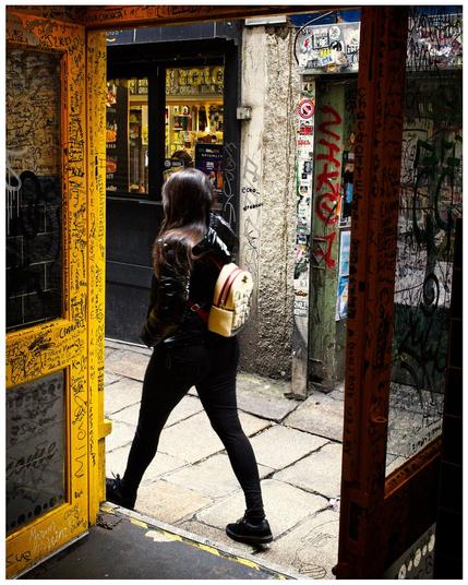 Woman framed by shop doorway. Shop and street are covered in graffiti.