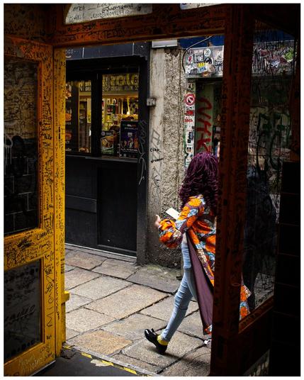 Woman framed by shop doorway. Shop and street are covered in graffiti.