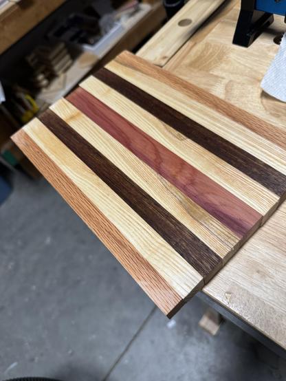 A cutting board with alternating stripes of different types of wood placed on a workbench.