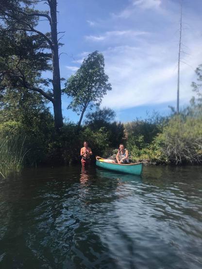 I am sitting in a green canoe, with a friend in the water behind me. On a lake. We've tied up canoe to a small islet.
