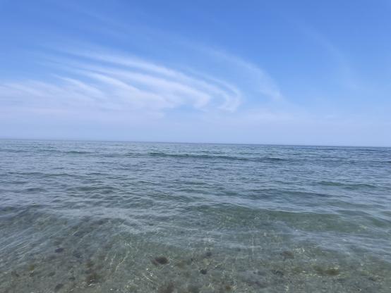 Calm ocean waves under a clear blue sky with streaked clouds.