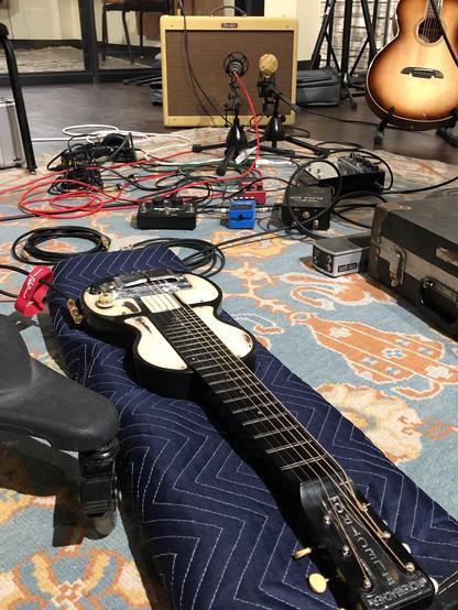 Lap steel guitar on floor in front of effects boxes, cables, and an amplifier.