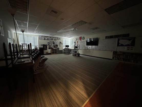 A dark, empty classroom with all the desks and chairs stacked.