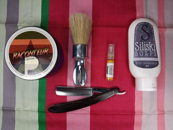 A pretty Victoria 4 straight razor with a tub of APR Raconteur, a Rubberset 400-3, a sample of Pharaoh's Dreamsicle frag and a squeeze bottle of Siliski's unscented balm