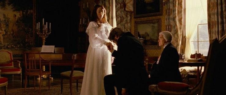 Two men kneeling before a young girl who stands before them in a nightgown. One man is taking her hand as he kneels, honoring her as the new queen