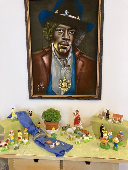 A "cascata" display of colorful hand-painted figurines on a landscape of green and blue cloth. A velvet painting of Jimi Hendrix looks skeptically down on the scene.