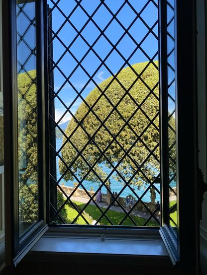 View thru a barred window down to a garden terrace and a dome-shaped tree at the Villa del Bslbianello