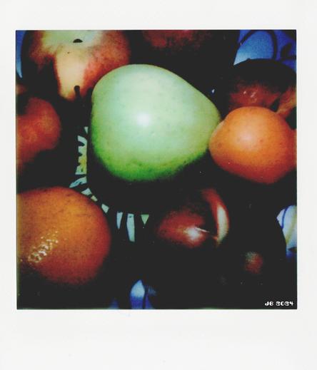 Instantfoto - Draufsicht auf eine Keramikschale mit Äpfeln, Pfirsichen, einer Orange, einer Aprikose und einer Nektarine.