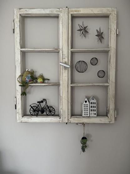 Ein altes, aufgearbeitetes Fenster als Deko an einer Wohnzimmerwand. Im Fenster sind einige Deko-Artikel angeordnet.