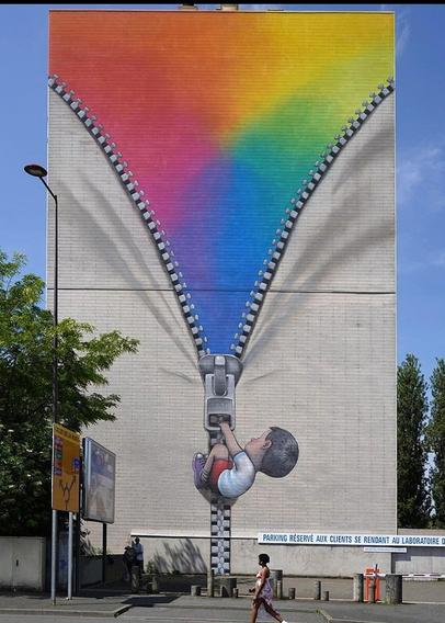 Streetartwall. On the outside wall of a nine-story building, a charming mural of a little boy has been sprayed/painted in a naive painting style. The little black-haired boy can be seen from behind, wearing a white T-shirt and red shorts, hanging from a large zipper that he pulls. The white fabric opens up and you can see a triangle in wonderfully bright colors. Simply beautiful. (In the photo, a passer-by is walking in front of the mural, surrounded by trees and traffic signs. A long sign for a visitor parking lot is a little distracting).
