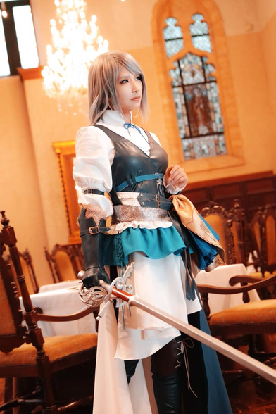 Xroserose in a Jill cosplay holding Jill's sword in her right hand. She stands in a well lit ornate room with vintage chairs and a stained glass window behind her.