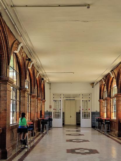 Pasillo del centro cultural la Térmica con ventanas en forma de arco. En un taburete se ve a una mujer hablando por teléfono.