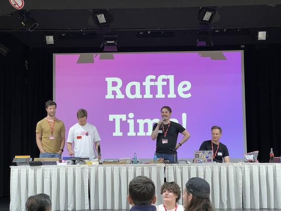 Es gab ein Gewinnspiel, hier sind vier Menschen auf der Bühne zu sehen, die Lose auswerten und Gewinne verteilen.