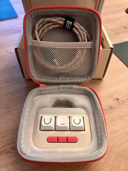 The opened carrying case shows the UwU macropad and a USB C cable in brown, pink and blue.

The macropad has three Cherry-style keycaps with the letters U, w and U. Below the keys there are three additional small buttons.