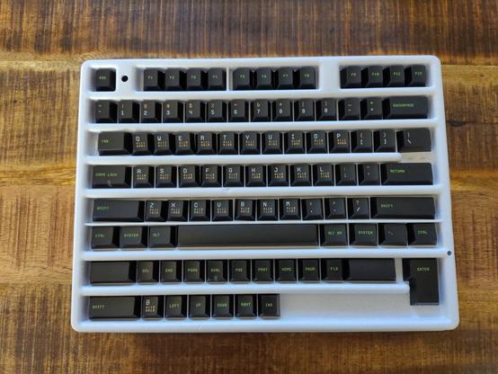 The keycap set inside the cardboard box. Function keys and modifiers are green, letters and symbols are white and brown. Eachbletter has it's binary code written in brown underneath