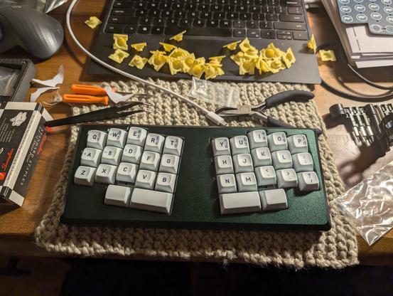 34-key, unibody split keyboard with Le Chiffre layout, in a rich green anodized aluminum case, on a desk with various tools and Topre parts strewn around it.