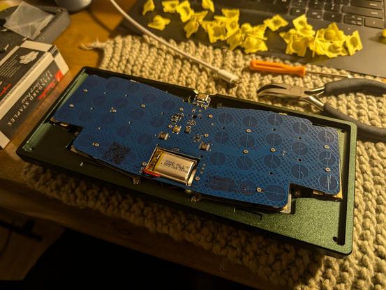 Exposed internals of the keyboard, showing the bottom of a blue PCB that includes a cutout for a thick LiPo pack in the center bottom portion.