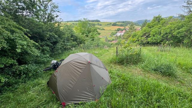 Zelt mit davorliegendem Fahrrad steht oben auf dem Berg mit herrlicher Aussicht