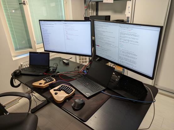 Desk with three laptops, two large monitors, a keyboard, and Ethernet cables connecting the machines.