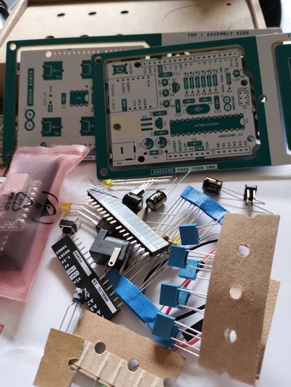 the unassembled parts poured on the table. at the top are the PCBs, to the left is the transparent bag with the USB C adapter and the Atmega microcontroller, at the bottom are all components for the Arduino Uno board on a pile