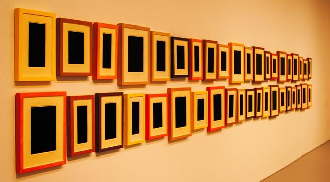 Color photo of a wall with two rows of frames with what could be matted  photos in them.  But each “photo” is just solid black.   
The camera viewpoint is from one end of the rows looking down towards the other end in the “distance”

Hirshhorn Museum @ The Smithsonian - Washington DC April 2012

Part of Dark Matters: Selections from the collection   Exhibition  Feb 2012 - Jan 2023