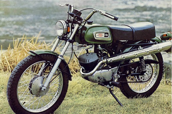 1971 Vintage Motorcycle on Display

The image displays a vintage motorcycle, likely from the 1970s, parked outdoors with a natural backdrop.
It has a classic design, featuring a prominent round headlight and a rectangular gas tank adorned with badges or logos.
The seat is small and flat, suggesting it is a single-seater model, possibly intended for touring or casual riding rather than long-distance cruising.