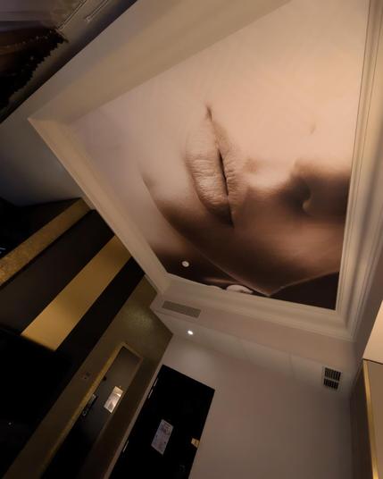 Image of a person's face with nose and lips visible (but not the eyes) on the ceiling above the bed in the hotel room.