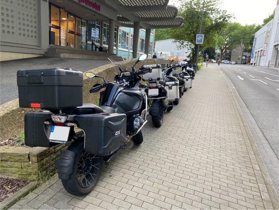 4 BMW-GS Motorbikes with Sidecases and Topcases parked in a row in front of a hotel. All Motorbikes have Portugese number plates.