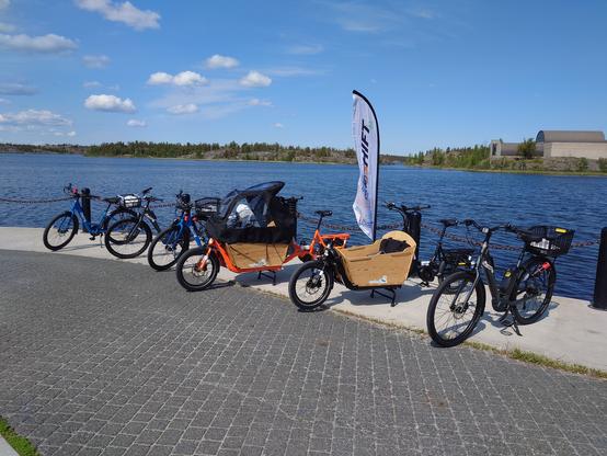 Bikes lined up against the shore of a lake with the Shift flag flying in the middle.