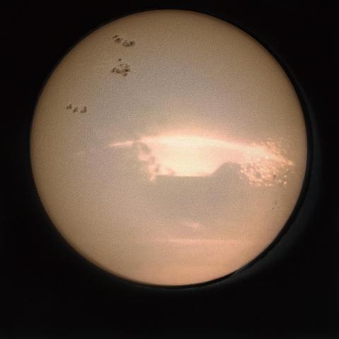 A sepia toned image showing silhouettes of trees and buildings, with the arc of the sun's passage shining behind them. Overlaid, sunspots and solar granulation.