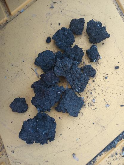 Black clumps of hard soil-like clumps resembling dirt clods on a yellow background.