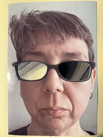 Collage in my sketchbook. A photo of a white woman’s face. She has short brown hair and rectangular glasses with dark frames. The lenses of her glasses have been cut out so that instead of her eyes, you see yellow lines wrapped gently around a yellow center on the left, and the same lines arcing around and down against a dark background on the right.