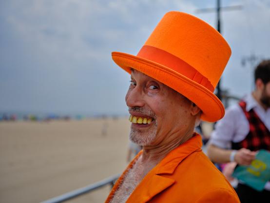 Individual in orange hat and suit participates in the celebratory Mermaid Parade at Coney Island, Brooklyn, bringing cosplay and costume to the beach and boardwalk.