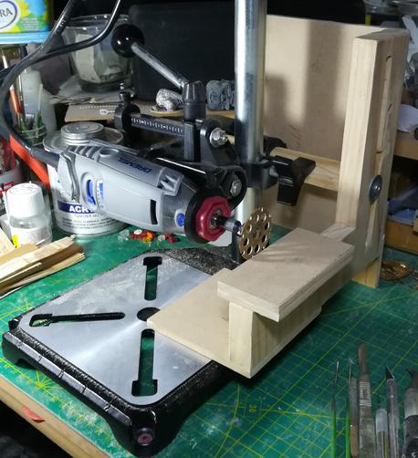 A dremel is mounted sideways on a drill press. A wooden jig is attached that allows cutting with the tool.