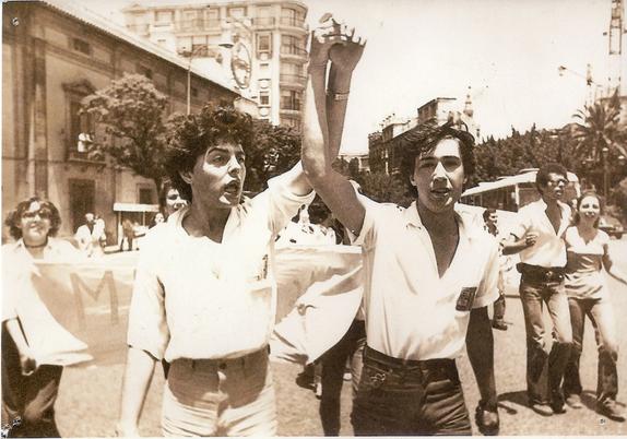 Dos personas avanzan en la manifestación con los puños en alto y cogiéndose las manos.
