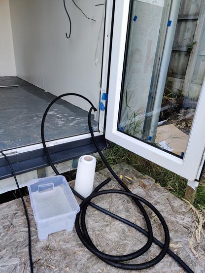 open door with two black cables (one armoured mains cable, the other conduit) coming through and sitting next to a bowl of hot soapy water and a roll of peeper towels.