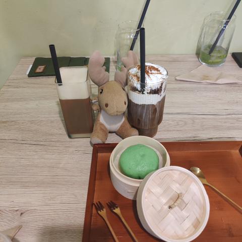 Mr Moose framed by a Vietnamese coffee in a square glass, an iced coffee with tiramisu, and ready to pounce on the green pandan bao in the steamer basket