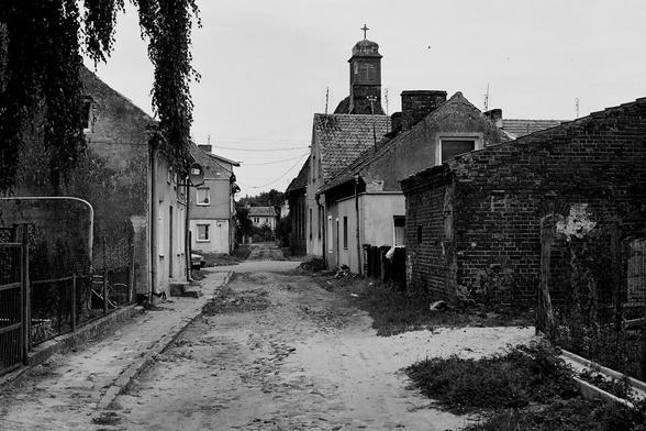 czarno-białe zdjęcie wiejskiej drogi, stare budynki po bokach / black-and-white photography of village road, old buildings on sides