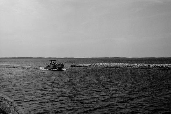 mała jednostka pływająca wchodzi do portu, zdjęcie czarno-białe / small vessel entering port, b&w photo