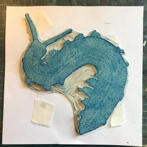 On a 8” x 8” square of white paper there’s a blue tinged irregularly shaped carved Lino block showing an S-shaped velvet worm, resembling a many-legged caterpillar with two antennas and a pattern of spots.