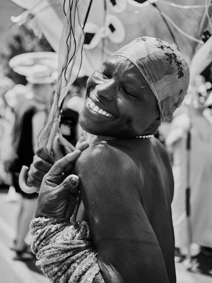 A participant at the Mermaid Parade in Coney Island, Brooklyn, smiles joyously in a costume, amidst the beach and boardwalk festivities.