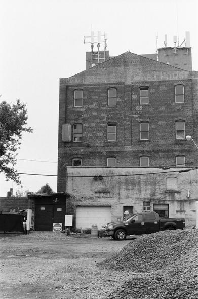 A truck sits behind a pile of rubble in a dirt lot below an old brick building