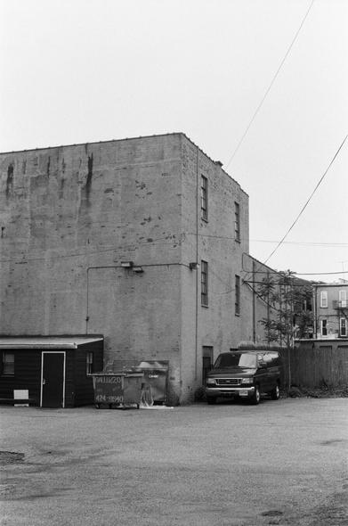 A van sits near a building in a dirt lot.